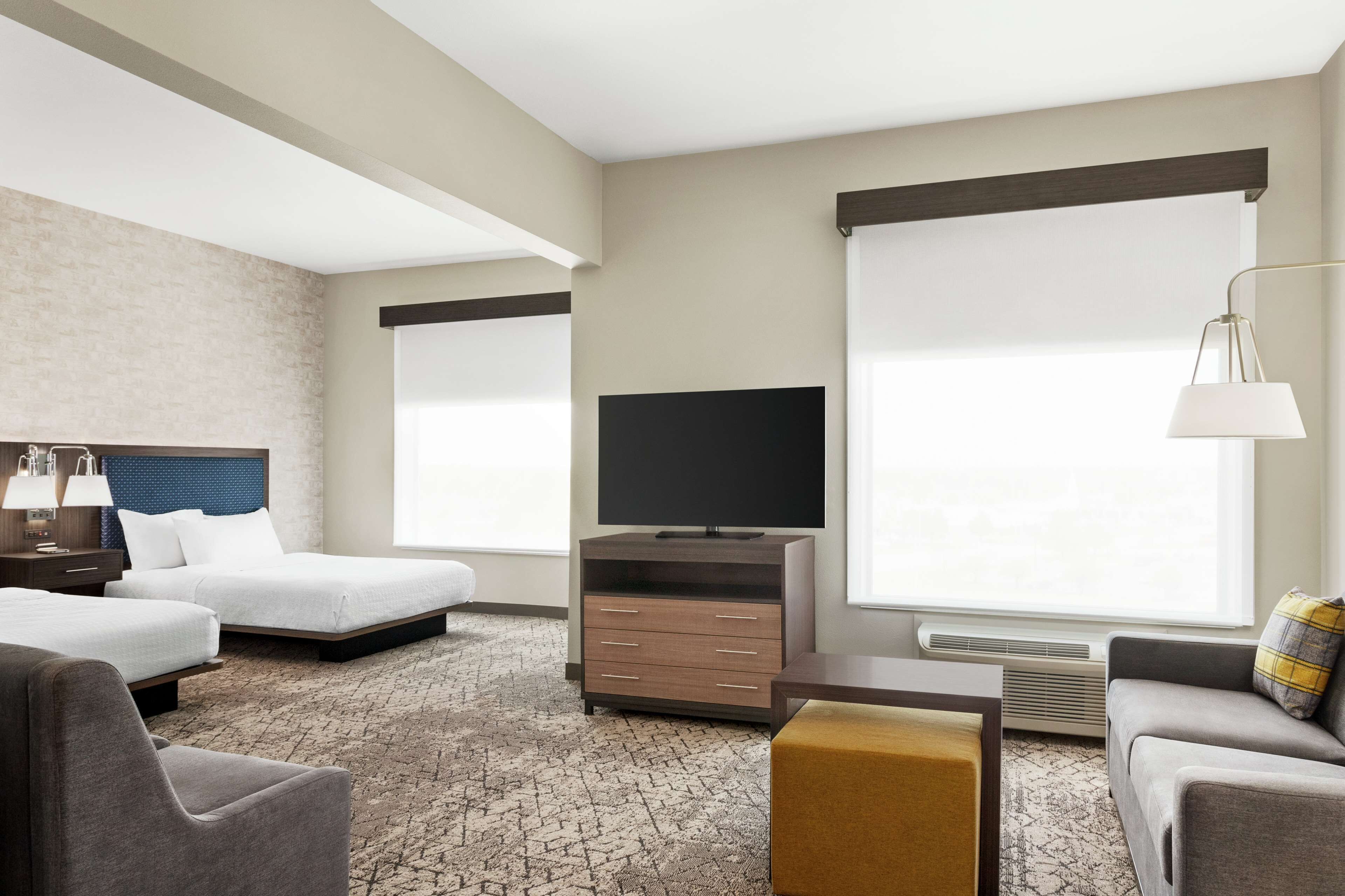 Quarto de hotel com duas camas, televisão, escrivaninha, cadeira e sofá.