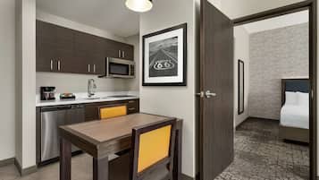A compact hotel room with a kitchenette, a dining area, and a bed.