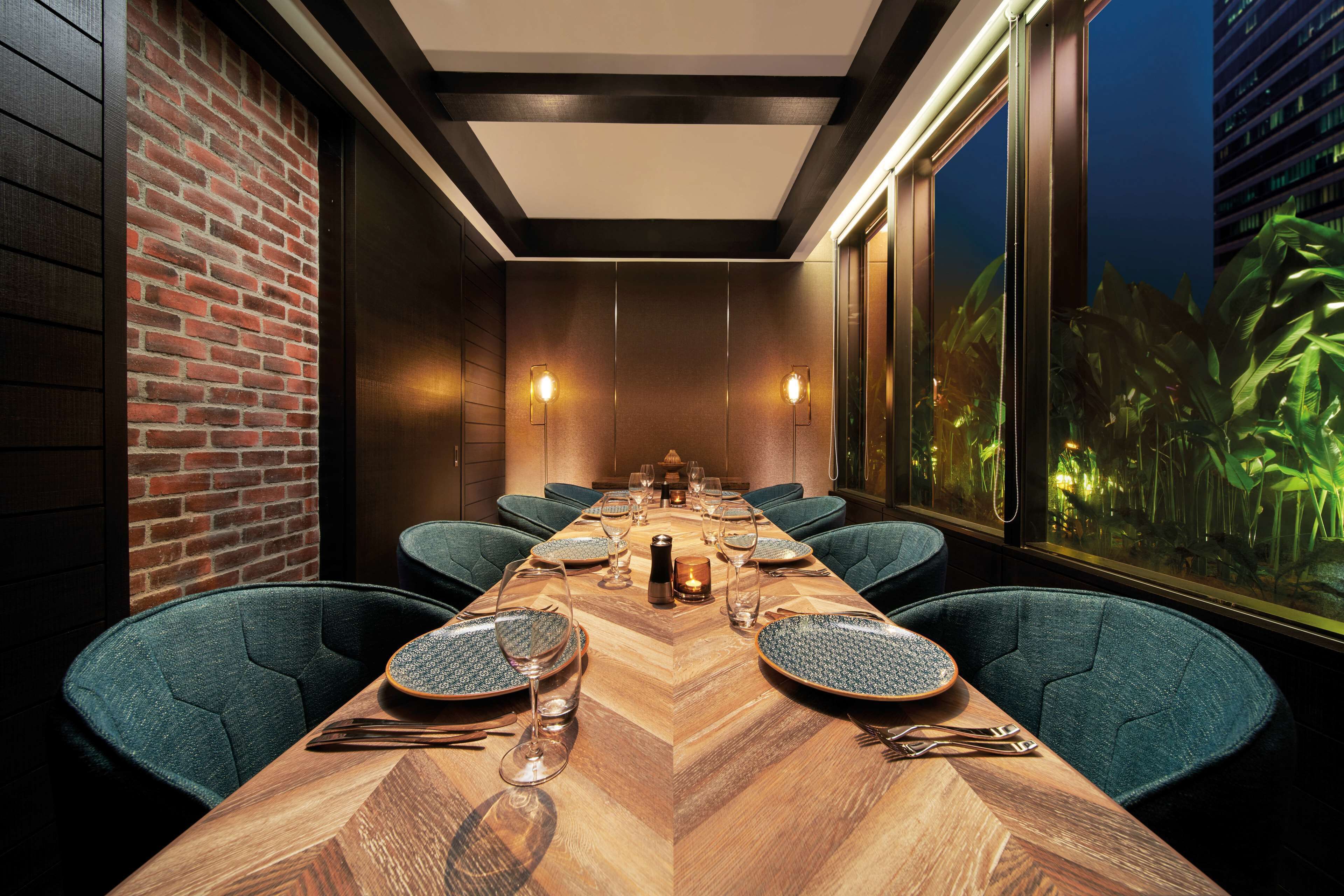Une salle de conférence avec une longue table en bois, des chaises recouvertes d’un tissu vert et un mur en briques.