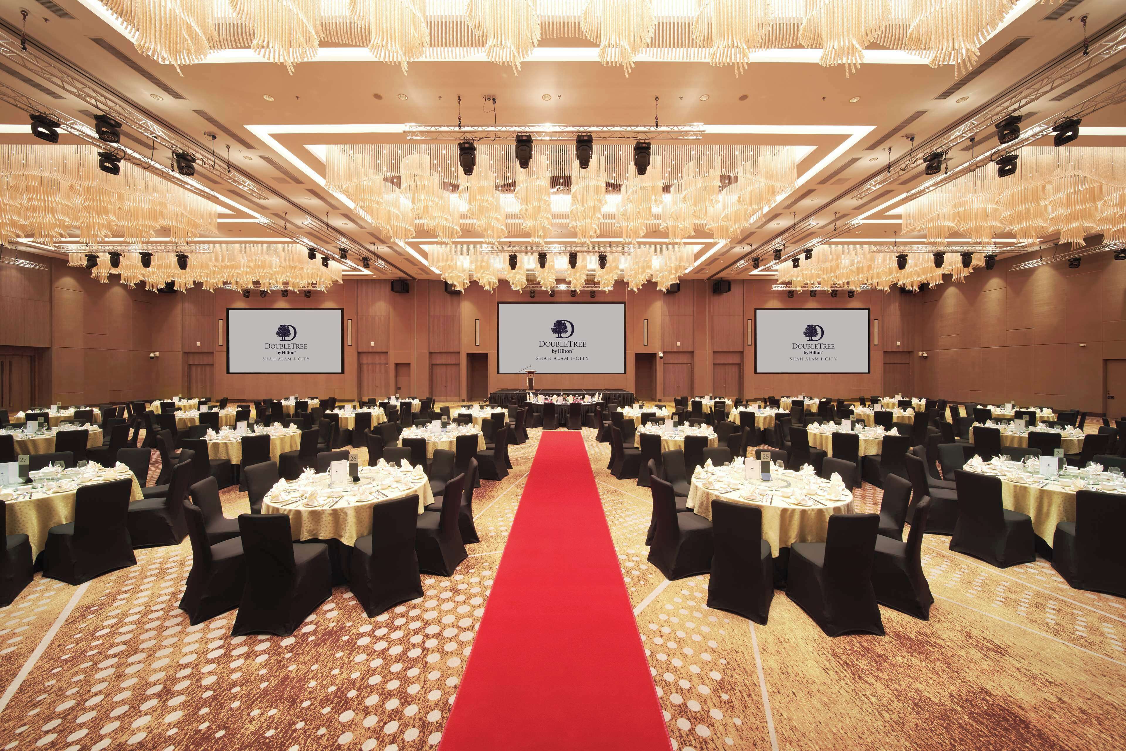 A large conference room with a red carpet, multiple tables with chairs, and a ceiling with hanging lights.