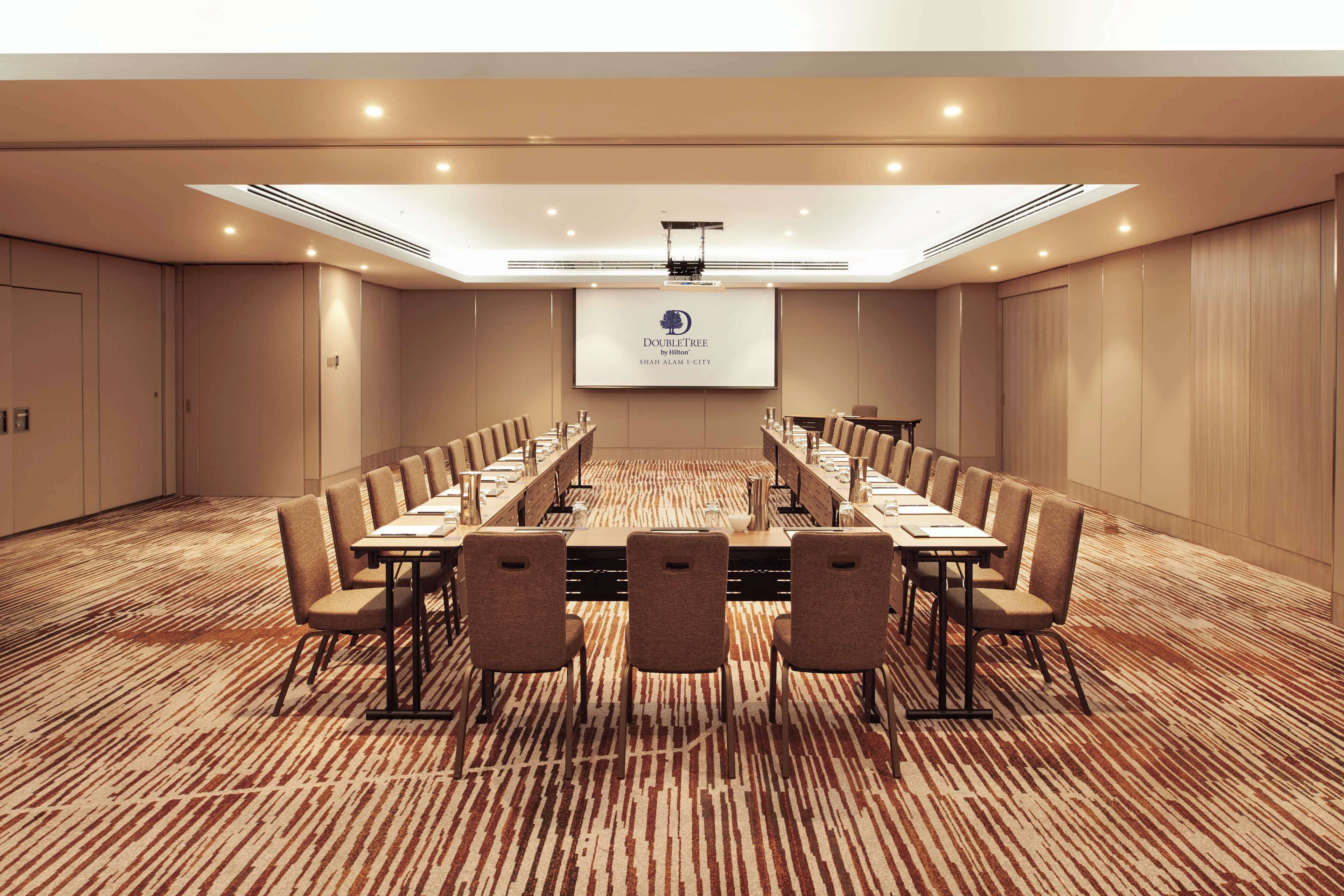 A conference room with a long table, chairs, a projector screen, and a carpeted floor.