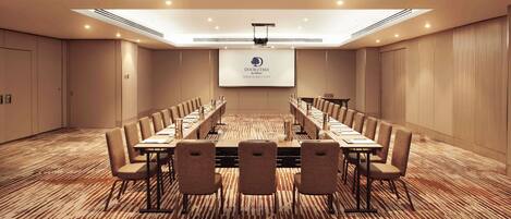 A conference room with a long table, chairs, a projector screen, and a carpeted floor.