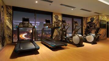 Un gimnasio con cintas de correr, elípticas y bicicletas estáticas, amplias ventanas con vistas a la ciudad y un diseño moderno.