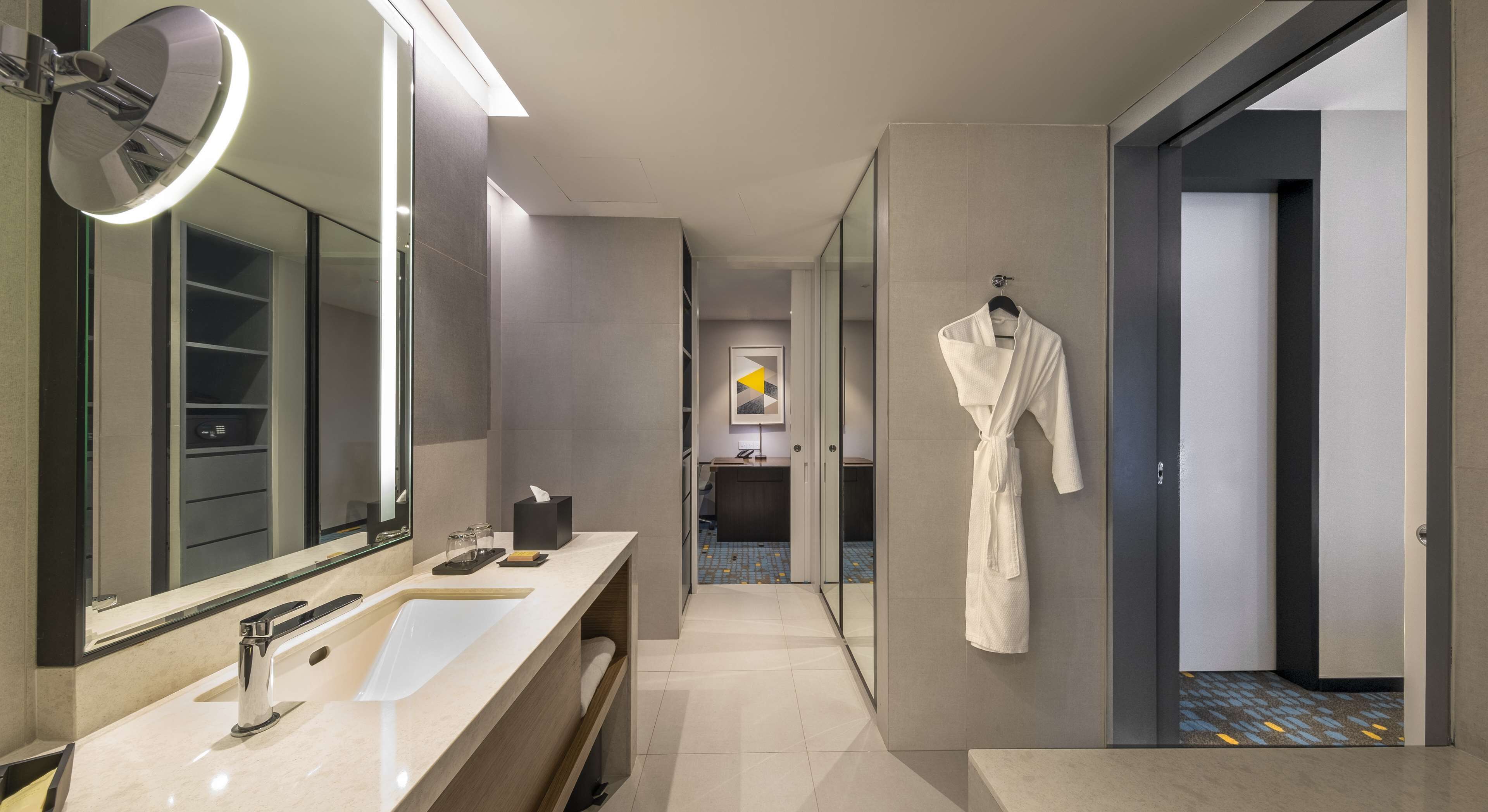 A modern bathroom with a large mirror, a vanity with a sink, and a robe hanging on the wall.