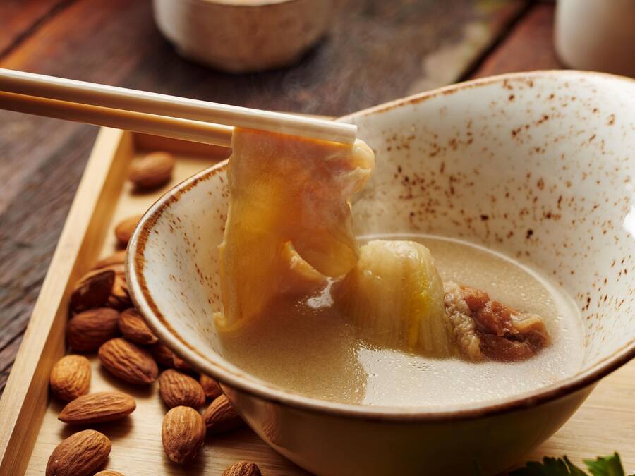 A bowl of soup with chopsticks, almonds, and parsley on a wooden tray.