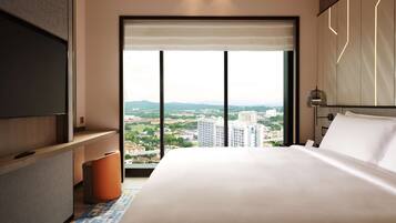 Habitación de hotel moderna con una cama grande, televisor y vista del paisaje urbano a través de ventanas de piso a techo.