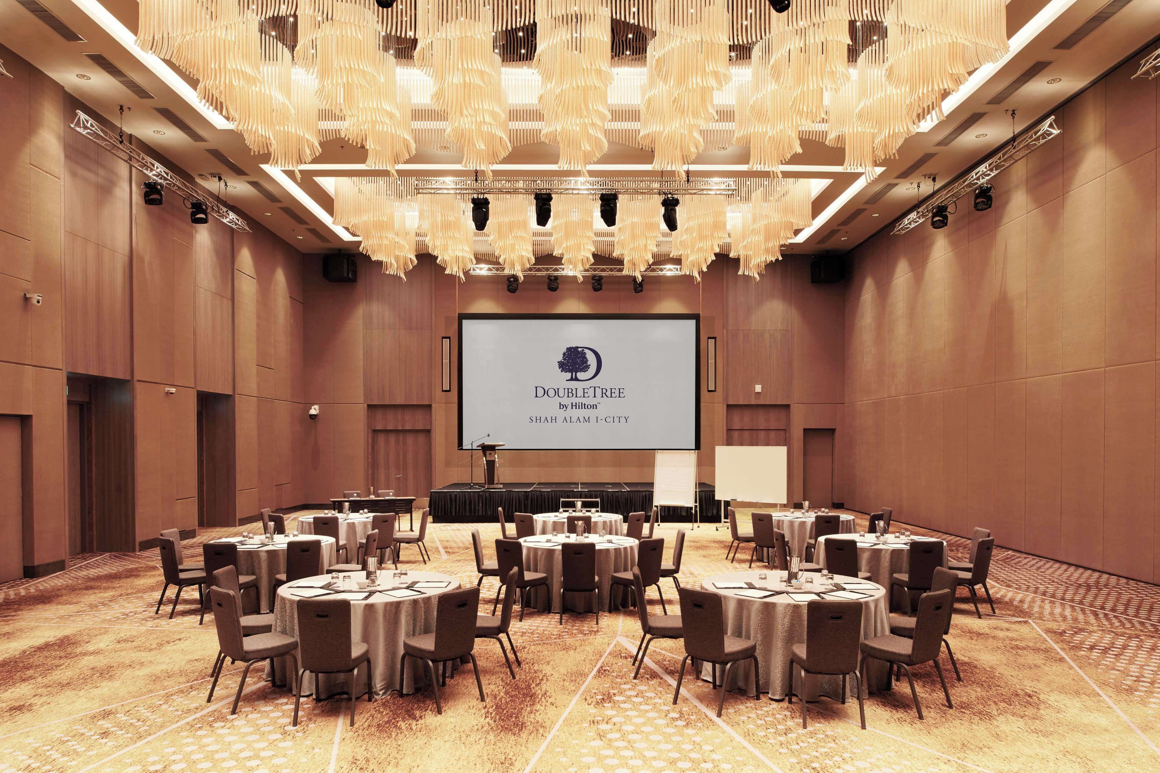 A conference room with round tables, chairs, a large screen, and a chandelier.