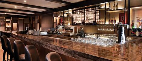 A bar area with a marble countertop, bar stools, and a well-stocked shelf with bottles and glasses.