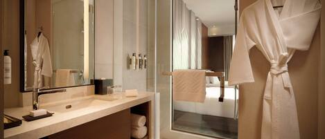 A modern bathroom with a glass shower enclosure, a large mirror, and a robe hanging on the wall.