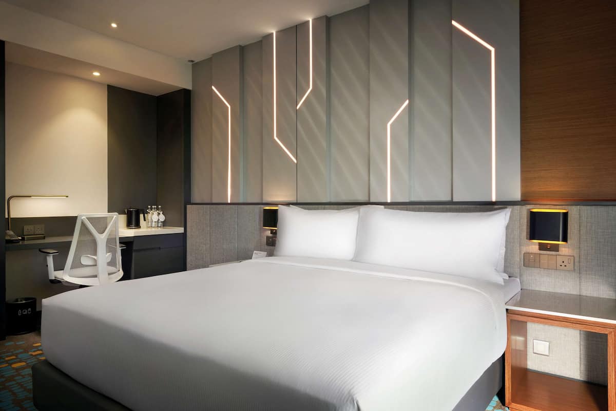 Una habitación de hotel moderna con una cama grande, un escritorio con silla, una mesita de noche y un televisor montado en la pared.