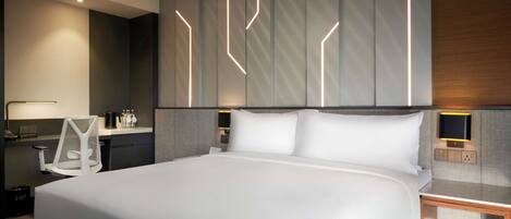 Una habitación de hotel moderna con una cama grande, un escritorio con silla, una mesita de noche y un televisor montado en la pared.