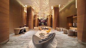A spacious lobby with a modern reception desk, comfortable seating areas, and a decorative chandelier.