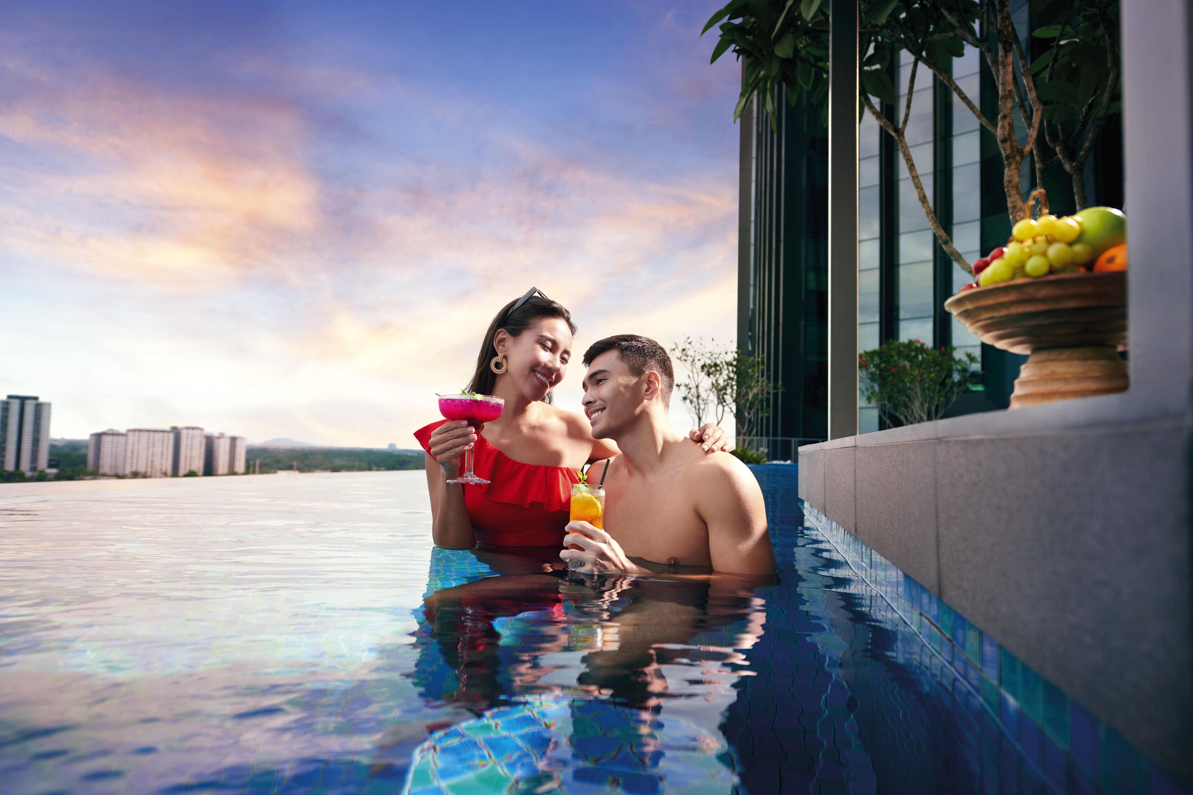 A couple in a swimming pool with a fruit bowl on the edge.