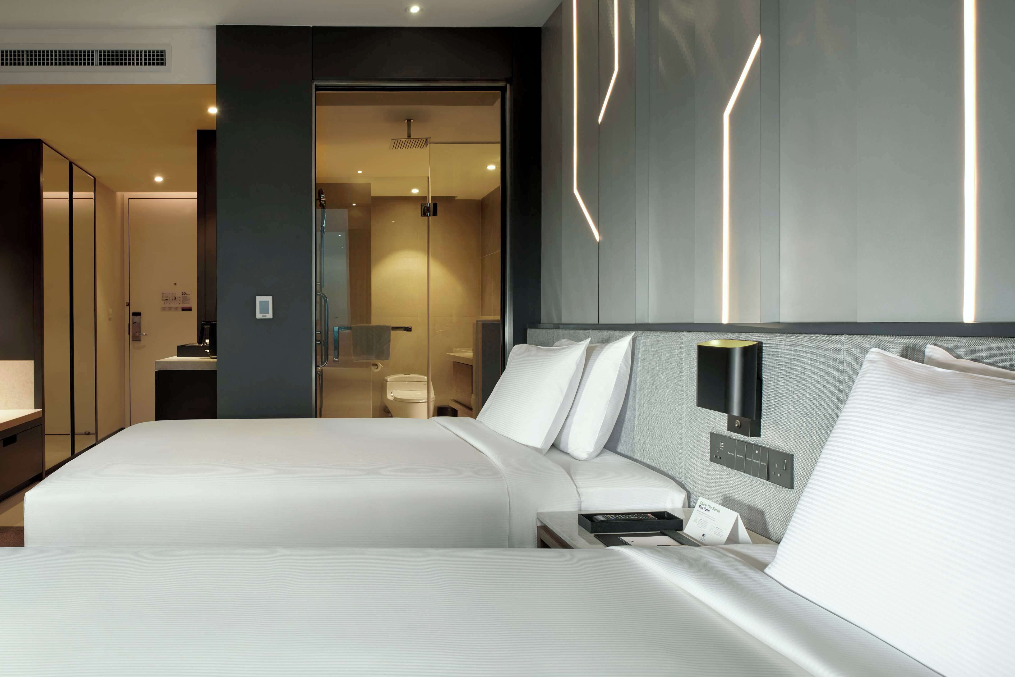Ein modernes Hotelzimmer mit einem großen Bett, Nachttischen, einem Spiegel und einem durchgegangene Tür erkennbaren Badezimmer.
