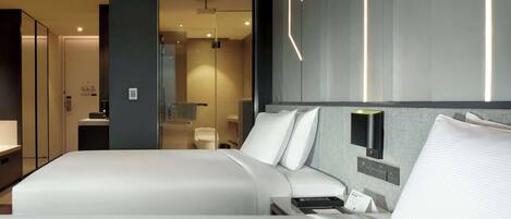 Ein modernes Hotelzimmer mit einem großen Bett, Nachttischen, einem Spiegel und einem durchgegangene Tür erkennbaren Badezimmer.