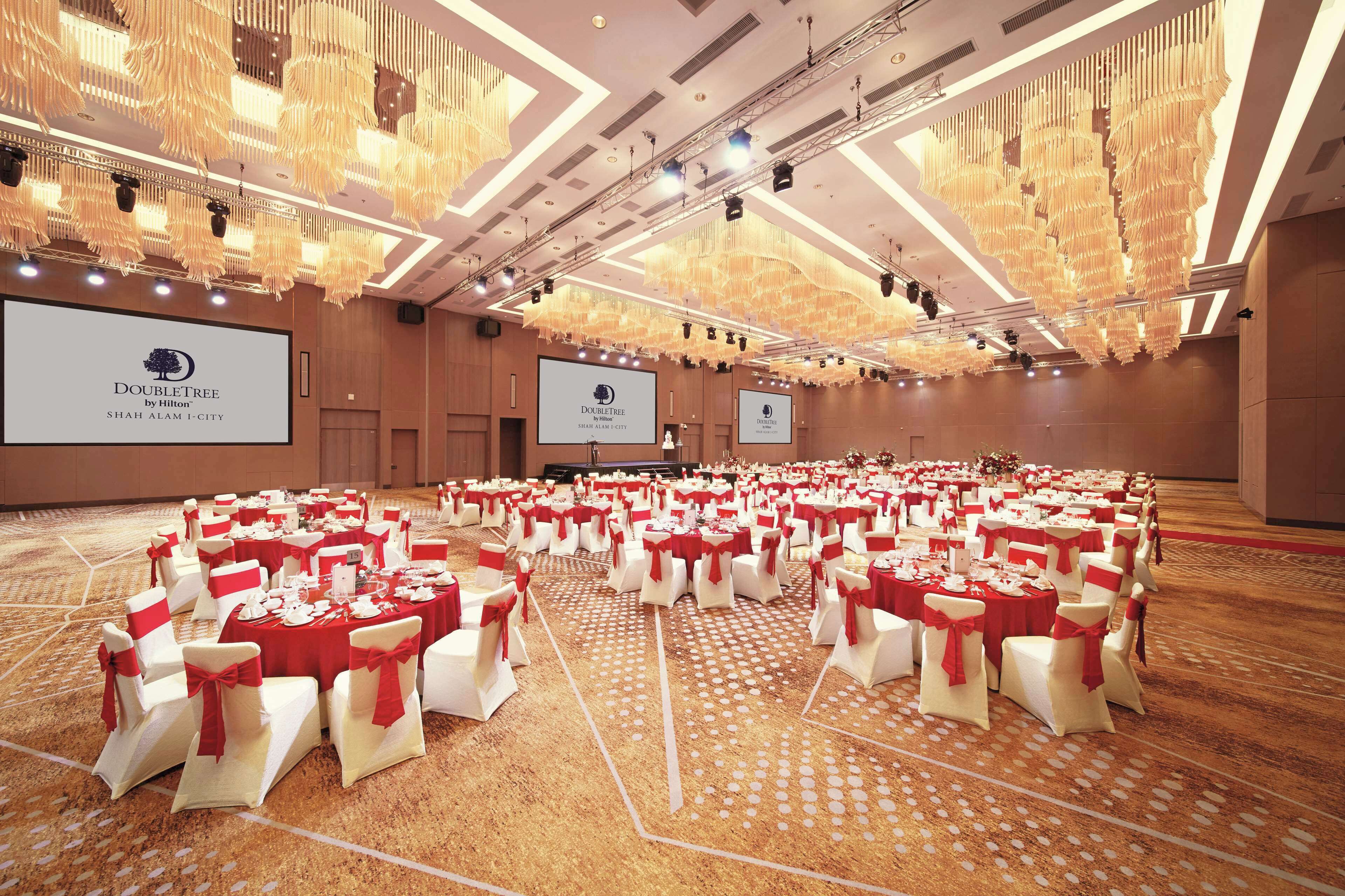 A large banquet hall with rows of tables set for a formal event, featuring a consistent theme with red and white color scheme.