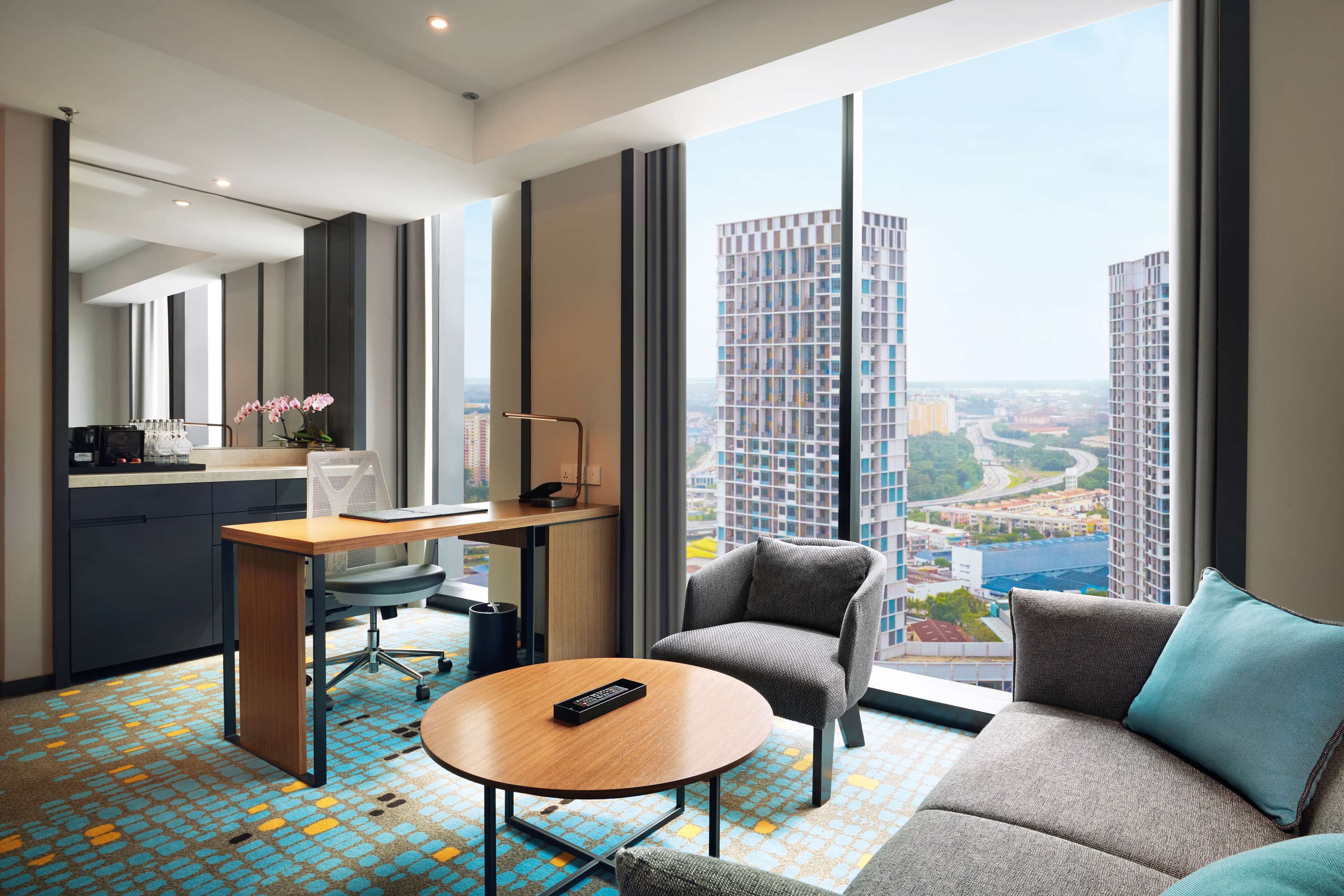 Habitación de hotel moderna con escritorio, silla, sofá y una ventana grande con vista a la ciudad.