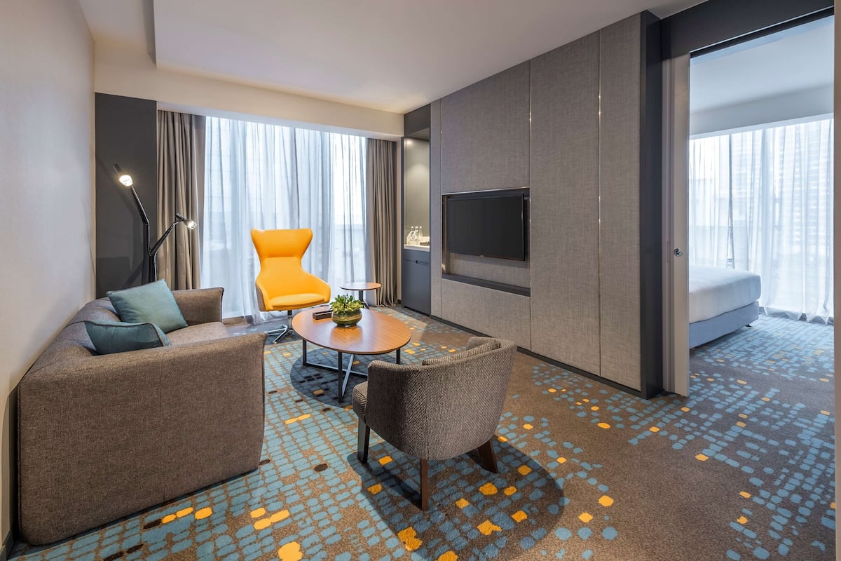 Una habitación de hotel moderna con sofá, sillón, mesa de centro y televisión fijada en la pared.