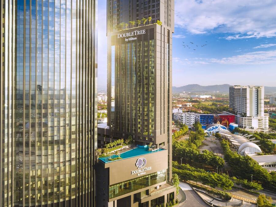 A high-rise hotel with a glass facade, named "DOUBLETREE by Hilton," featuring a rooftop pool and lush landscaping.