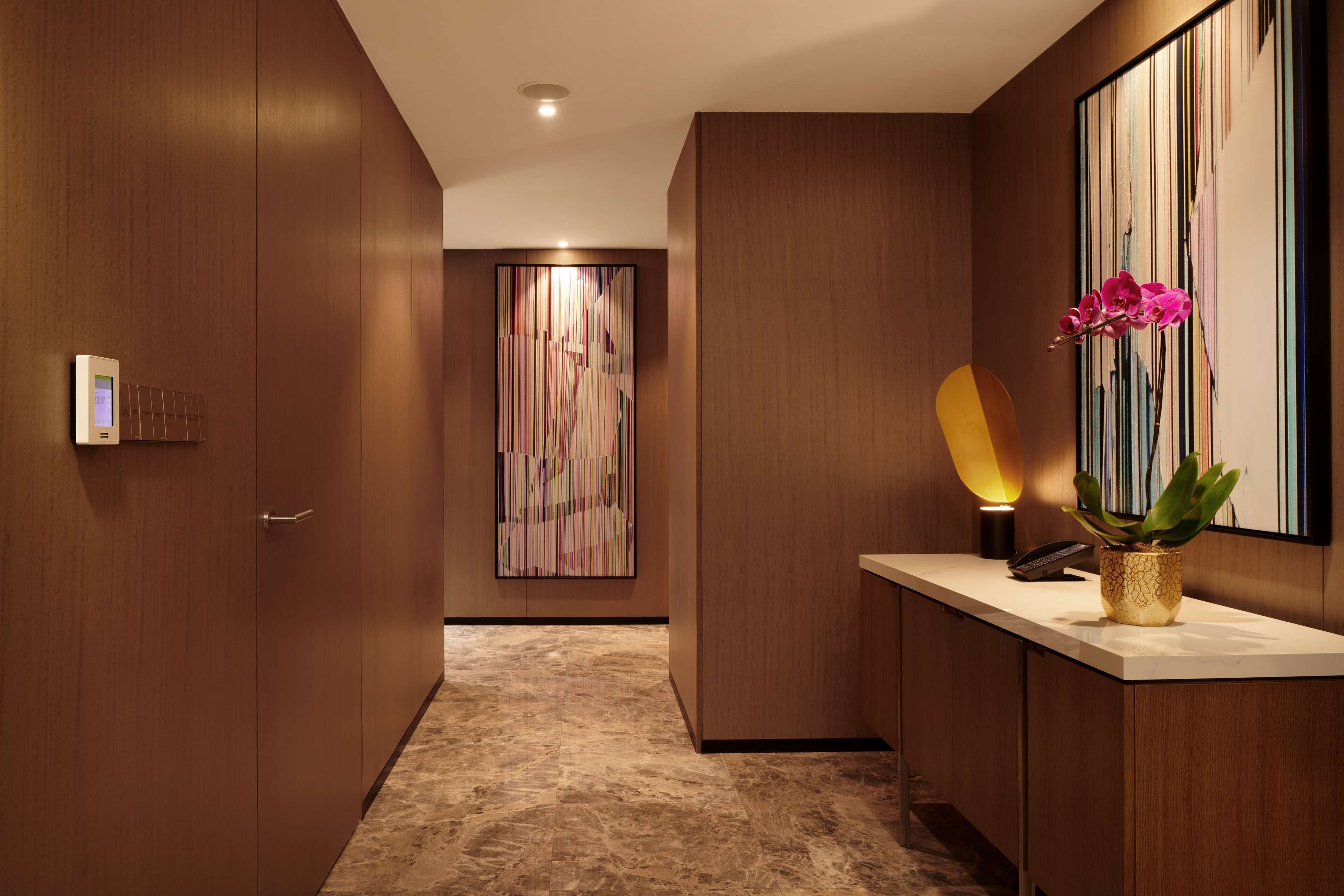 Un pasillo con paneles de madera, un mostrador de recepción, un teléfono, un jarrón con flores y un cuadro abstracto moderno en la pared.