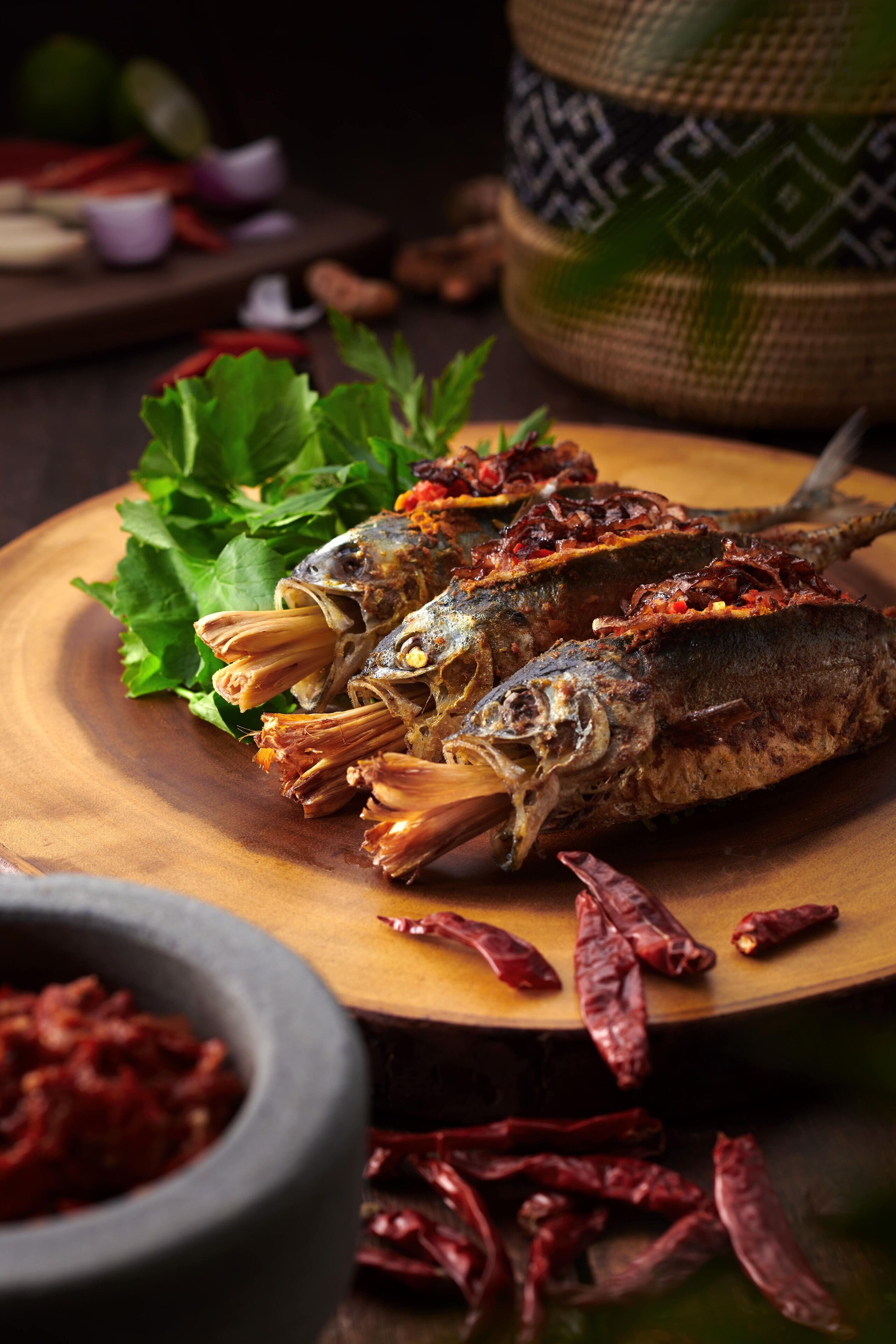 A wooden table with grilled fish, garnished with herbs and red chili peppers.