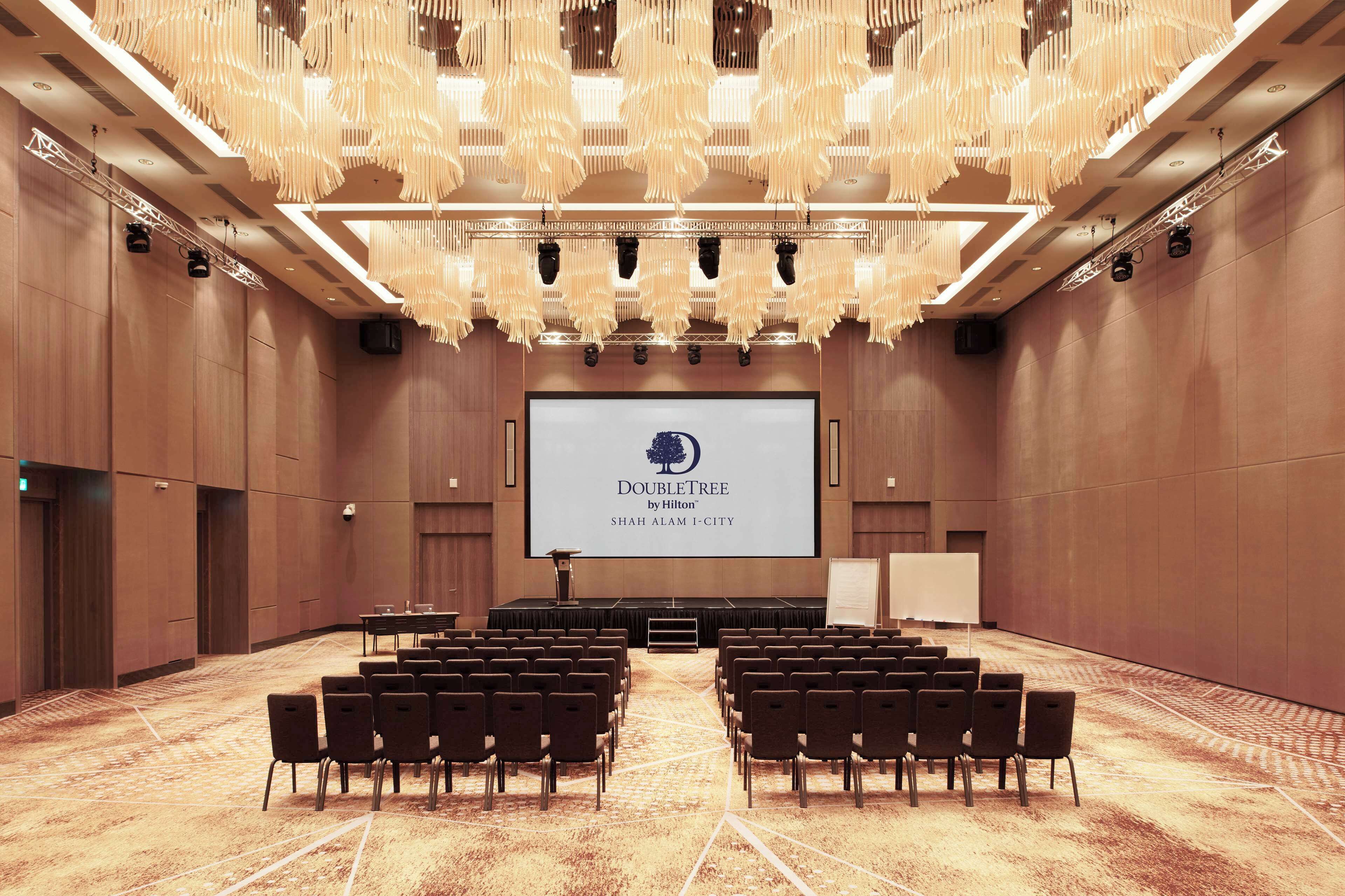 A conference room with rows of chairs, a large screen displaying the DoubleTree logo, and a modern chandelier.