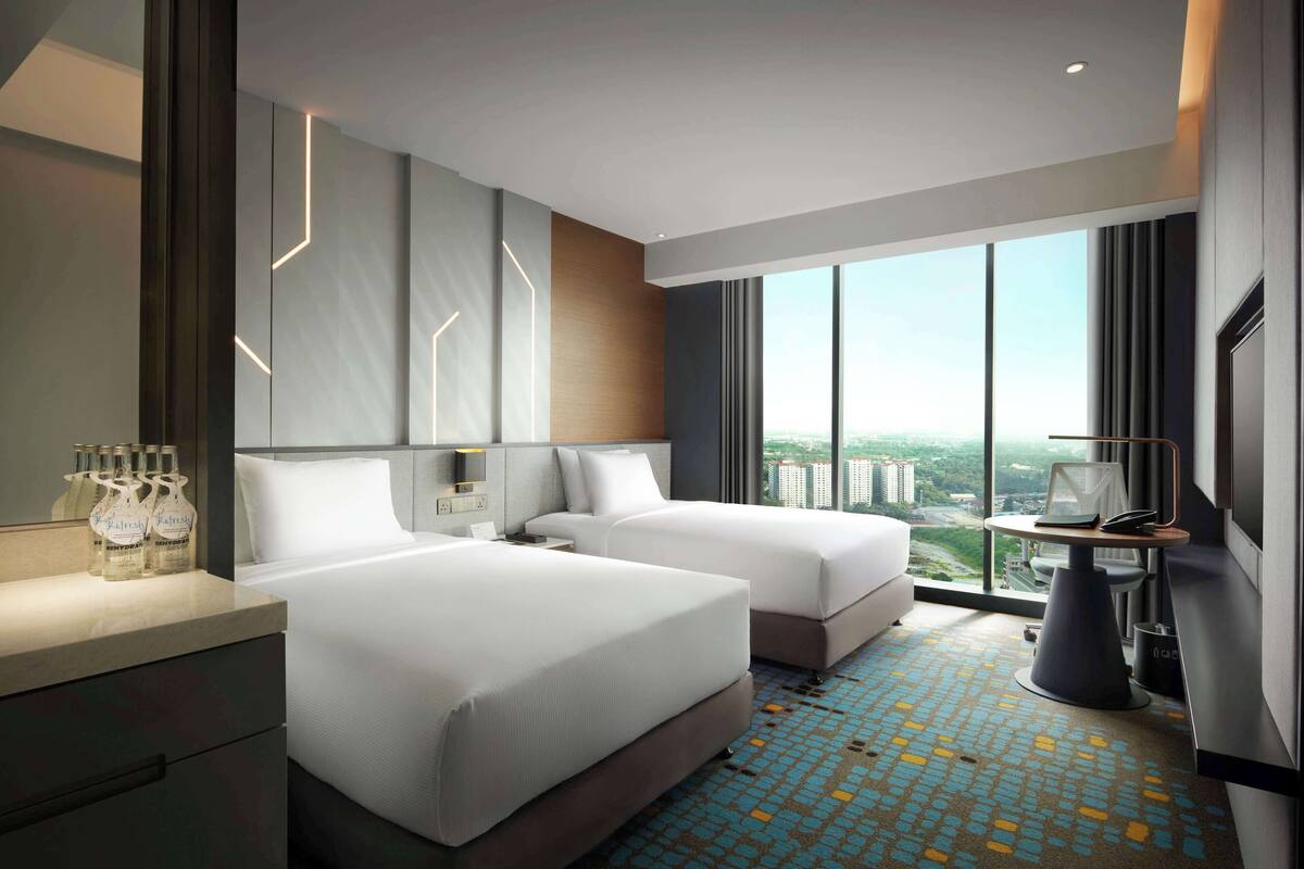 Una habitación de hotel moderna con dos camas, un ventanal grande con vistas a la ciudad, un escritorio con una silla y un minibar.