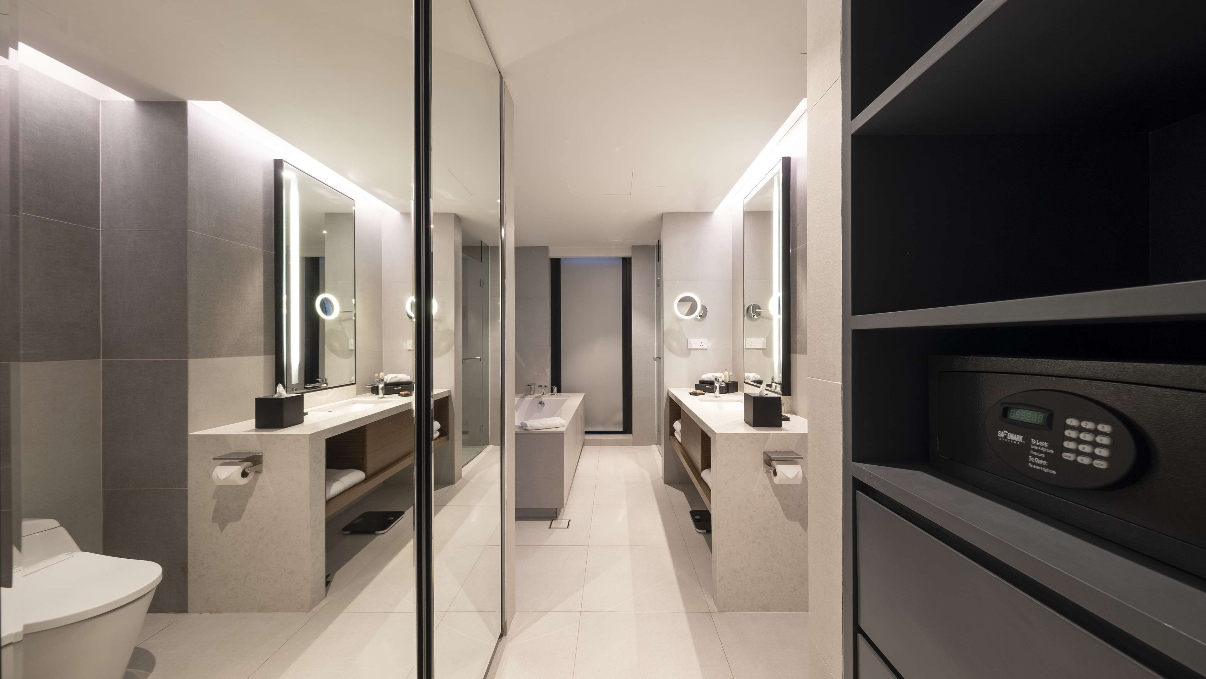 Une salle de bain moderne dotée de deux lavabos, de toilettes et d’une douche. Elle est équipée d’une serrure numérique et d’un miroir avec éclairage intégré.