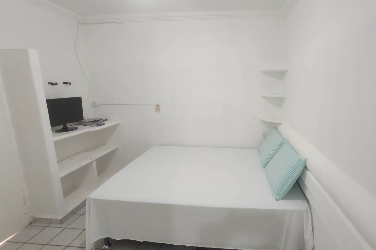 Una habitación pequeña con una cama individual, un escritorio y estanterías.