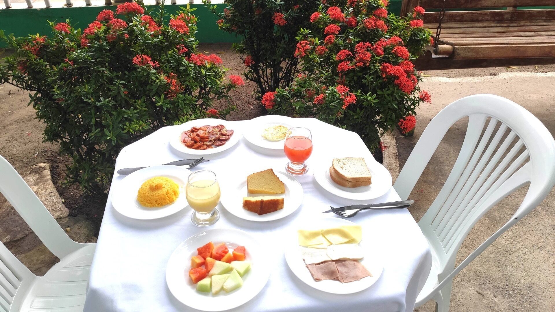 A table set outdoors with plates of food, including fruits, bread, and a glass of juice.