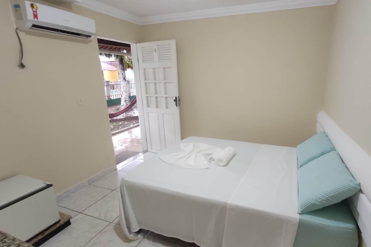 Una habitación pequeña y limpia, con cama, aire acondicionado blanco y puerta que da a un espacio exterior.