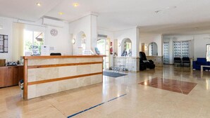 A hotel reception area with a reception desk, seating area, and a view of the lobby. - Mariners Club Apartments (Alcúdia)