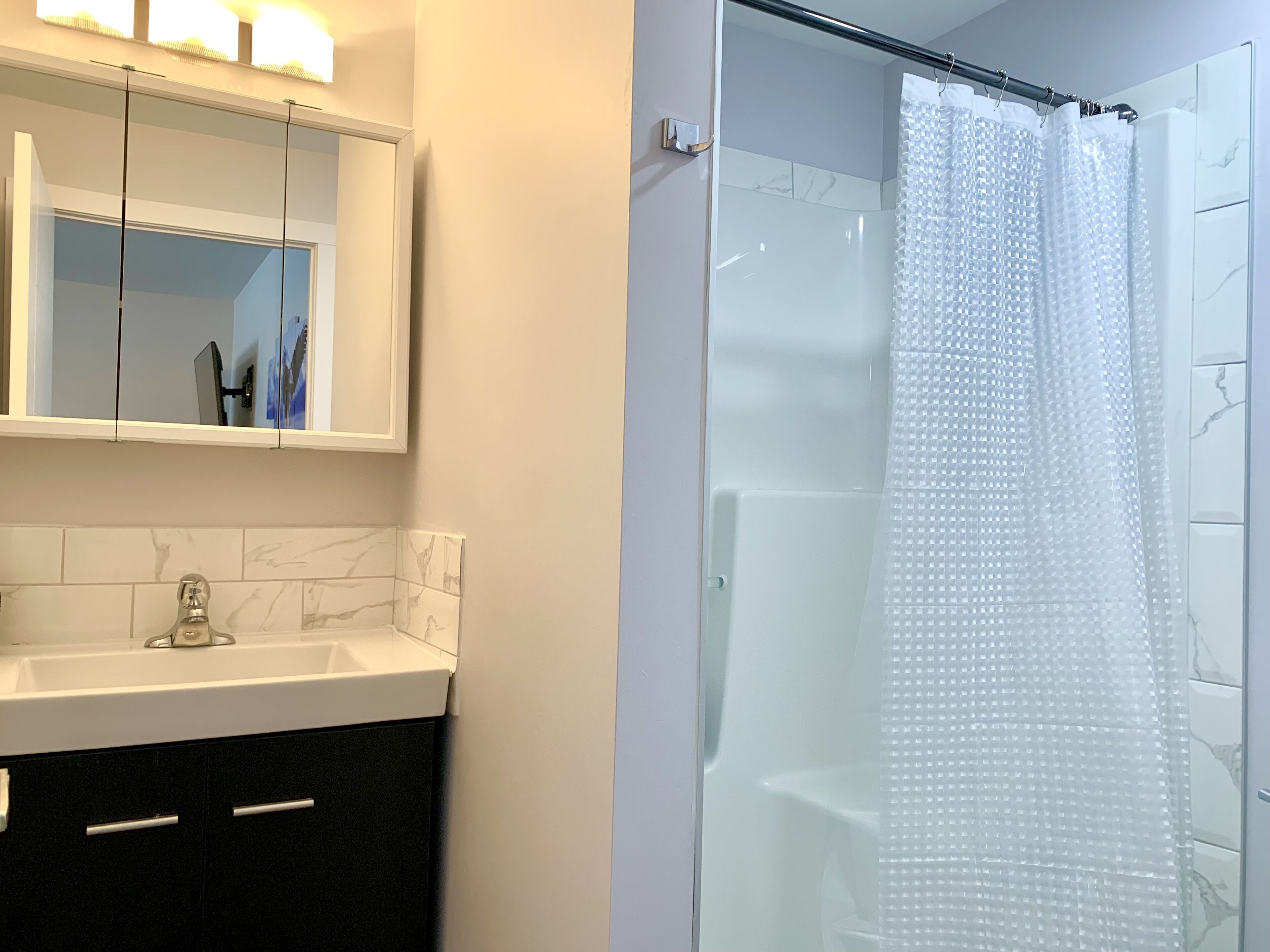 A modern bathroom with a glass shower enclosure, a marble-tiled vanity, and a mirror with lights above.