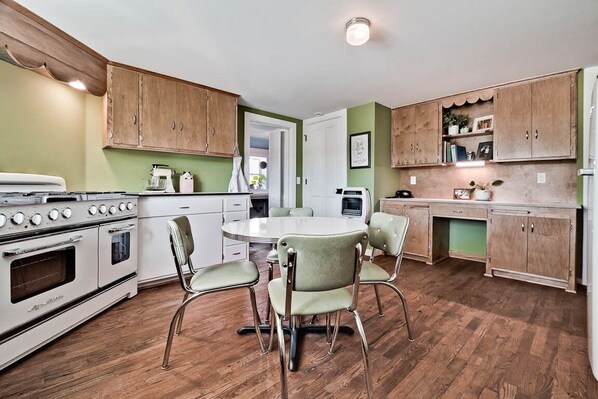 Une cuisine avec des meubles de rangement en bois, une cuisinière blanche et une table à manger avec des chaises.