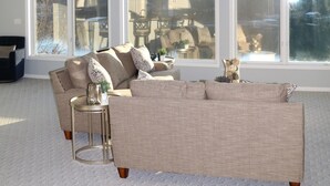 Un salon spacieux avec un grand canapé d’angle, une petite table ronde et un ventilateur de plafond.