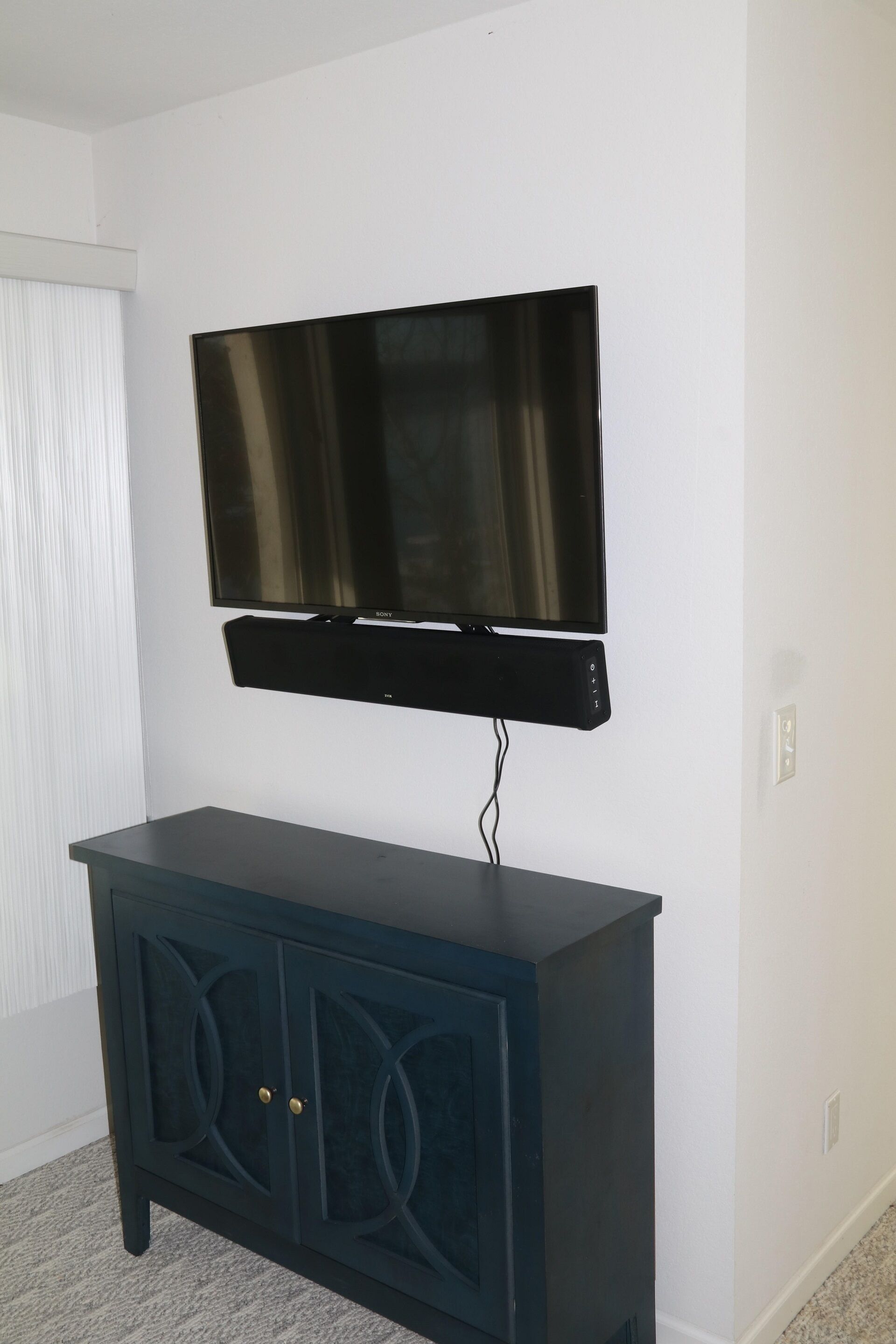 A flat-screen TV mounted on a dark blue cabinet with two doors, against a white wall.
