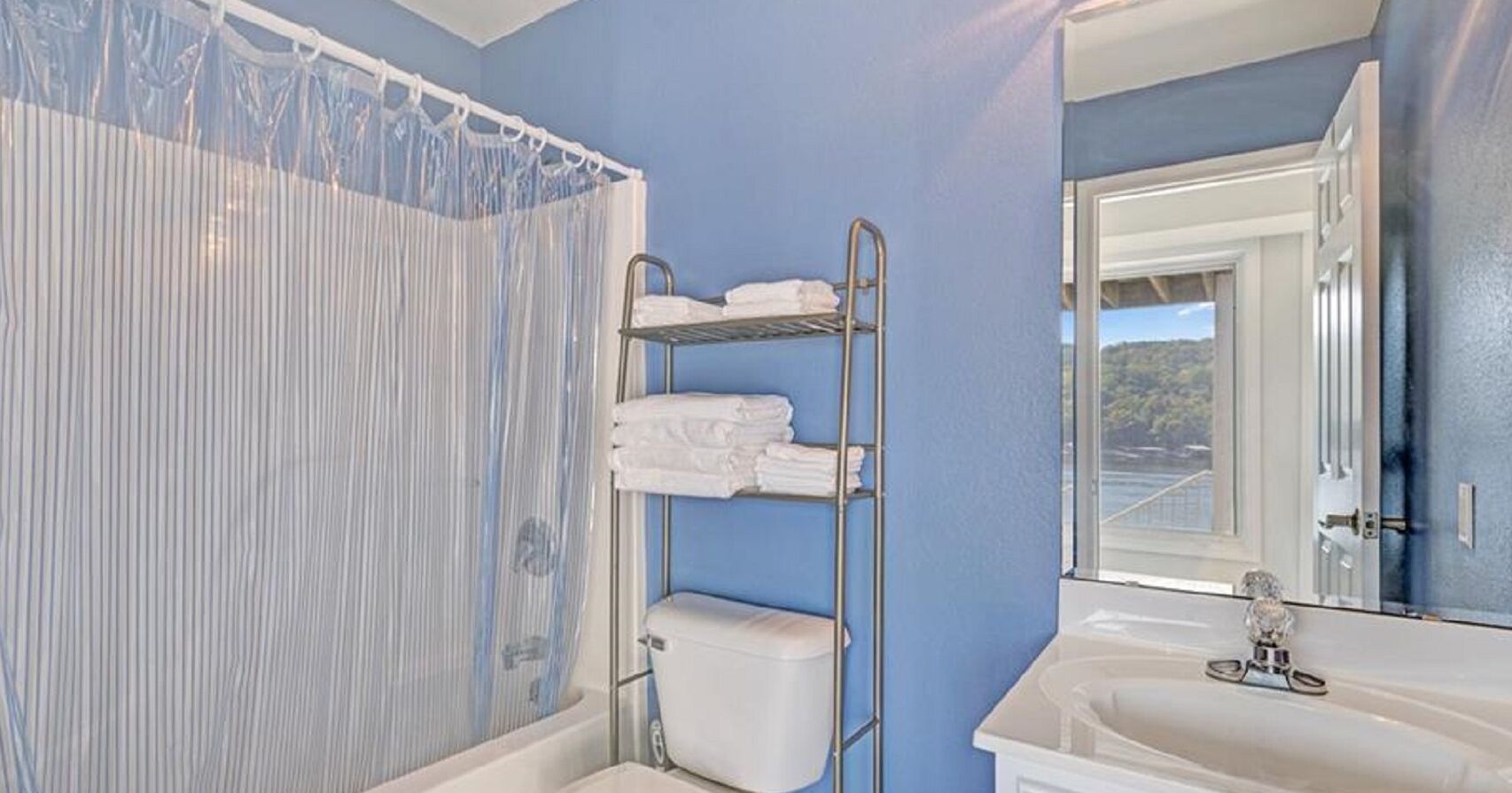 Un baño con pared azul, cortina de ducha, inodoro, lavabo y espejo.