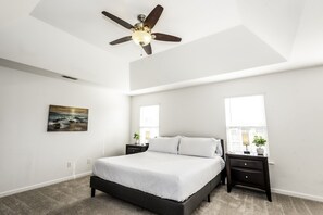 A bedroom with a bed, a ceiling fan, a nightstand with a lamp, and a window with blinds.