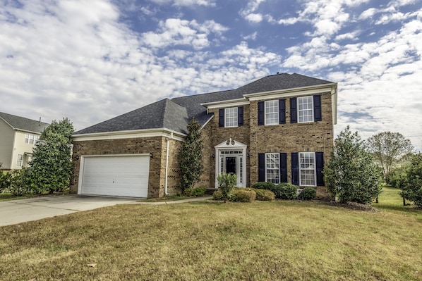 A two-story brick house with a garage, a front porch, and a well-maintained lawn.