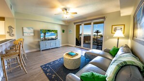 A spacious living room with a large gray sofa, wooden chairs, a round coffee table, and a ceiling fan. - EMERALD OASIS IN THE HEART OF PCB!  (Panama City Beach)