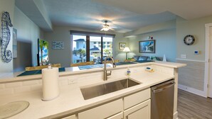 A modern kitchen with a stainless steel sink, white cabinets, and a dishwasher. There is a window providing a view of the outside. - EMERALD OASIS IN THE HEART OF PCB!  (Panama City Beach)