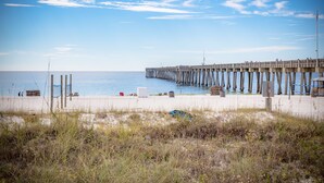 A pier extending into the water with a sandy beach in the foreground. - EMERALD OASIS IN THE HEART OF PCB!  (Panama City Beach)