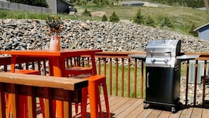 Una terraza de madera con una parrilla, sillas anaranjadas y una mesa.