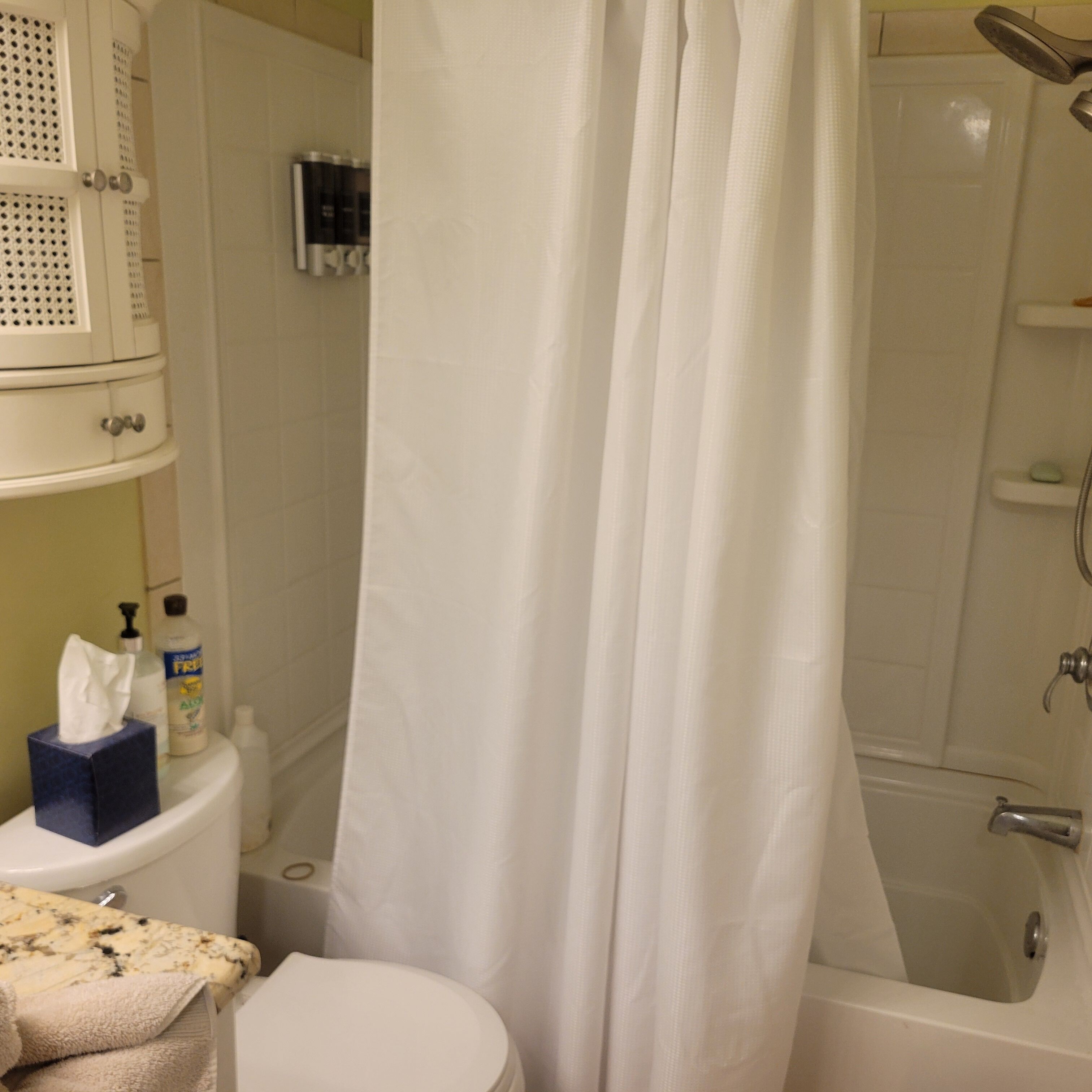 A bathroom with a toilet, a shower, and a bathtub. There are toiletries on the sink and a towel on the floor.