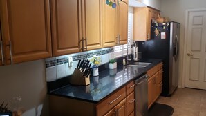 Una cocina con armarios de madera, encimera negra, refrigerador de acero inoxidable y un lavabo.
