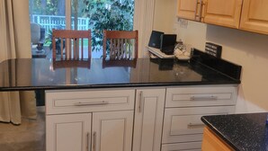 Una cocina con un ventanal grande, armarios de madera, encimera negra y una pequeña mesa con sillas.