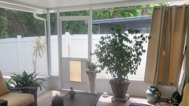 Un patio cubierto con mobiliario de mimbre, plantas en macetas y vistas al exterior.