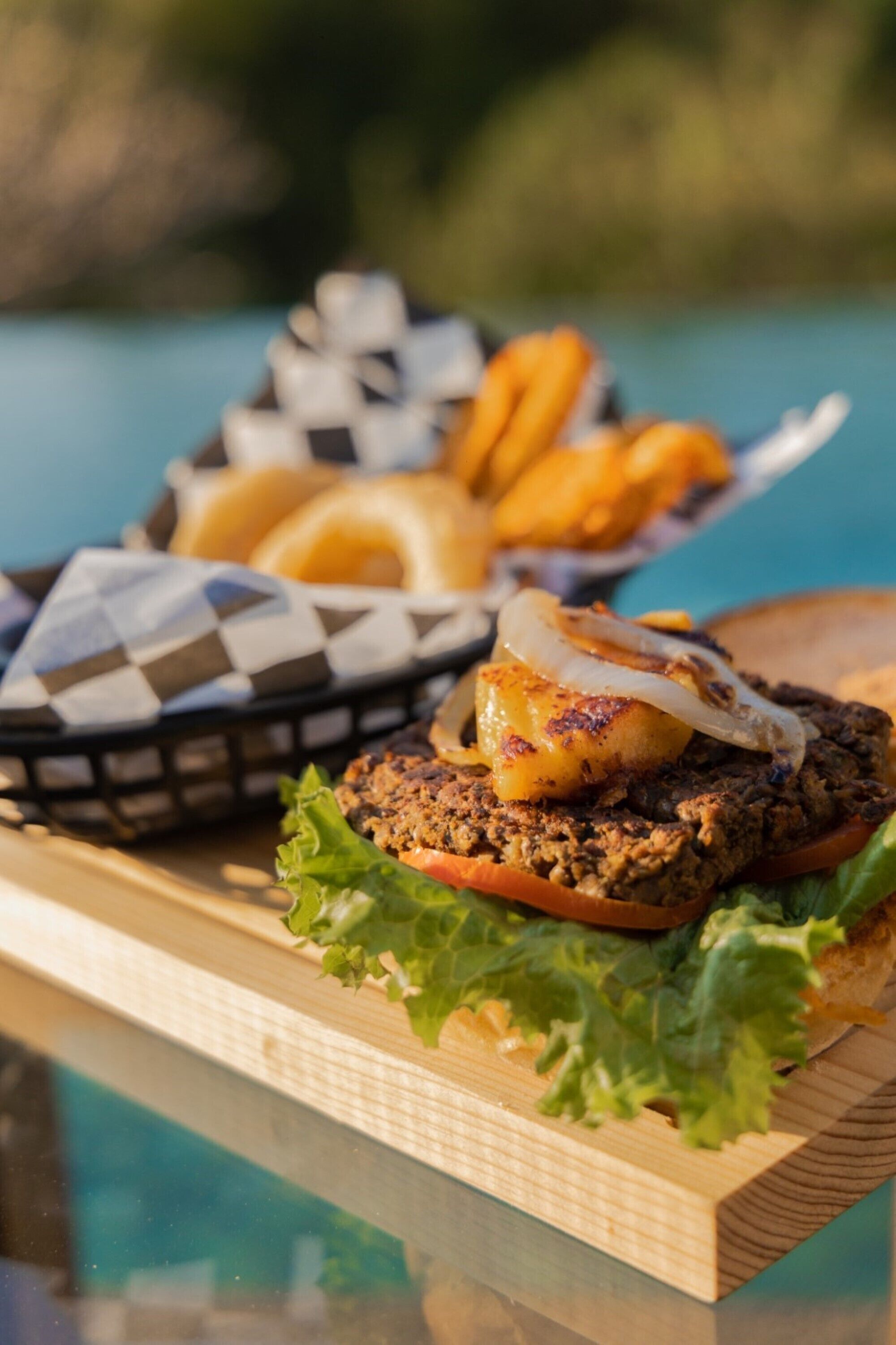 Een hamburger met een gegrilde burger, sla, tomaat en ui op een houten plank.