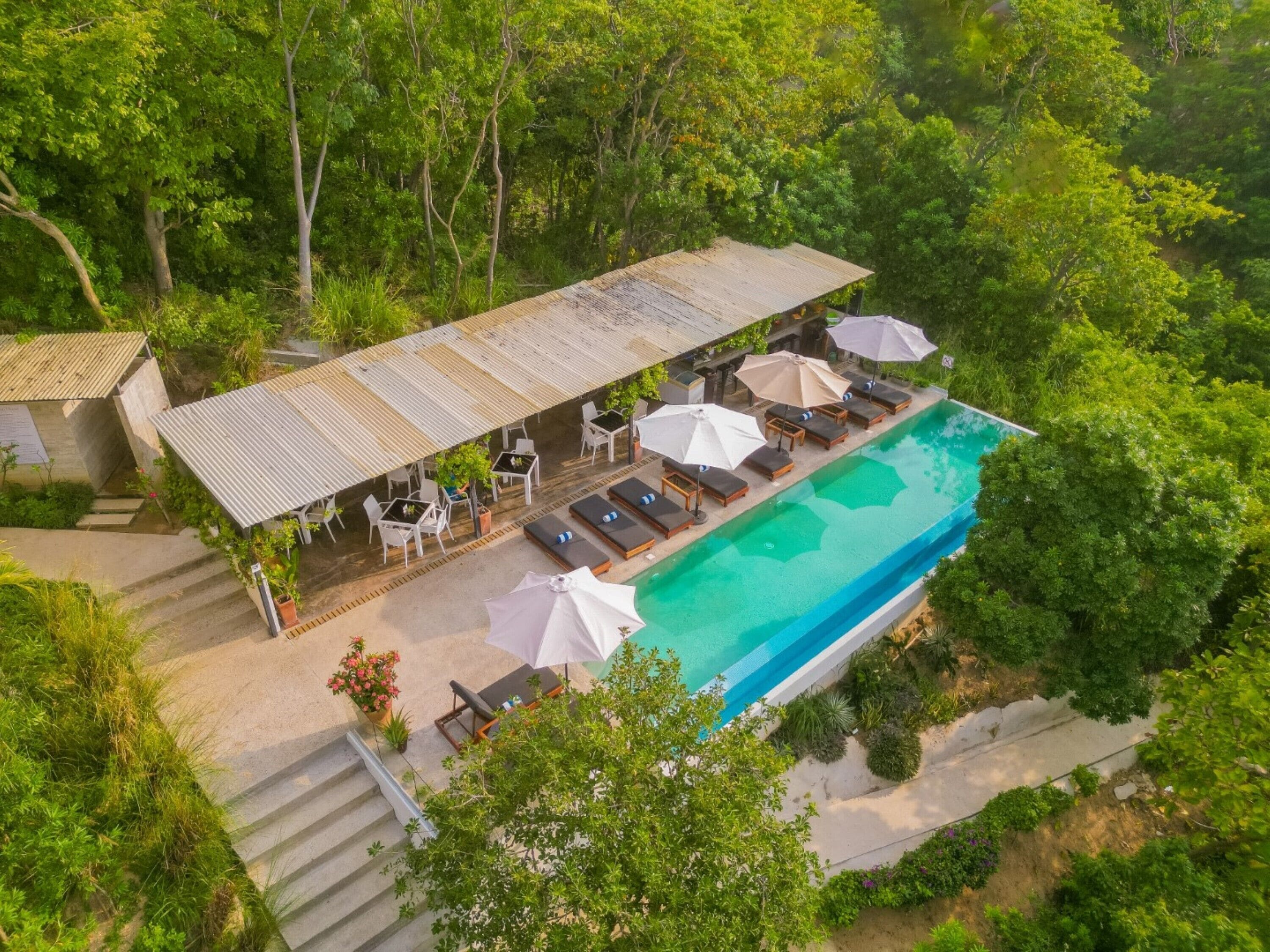 An aerial view of a resort with a swimming pool, lounge chairs, and umbrellas.