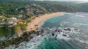 Vue aérienne d’une station balnéaire avec des propriétés situées en bord de mer, un littoral rocheux et une végétation luxuriante.
